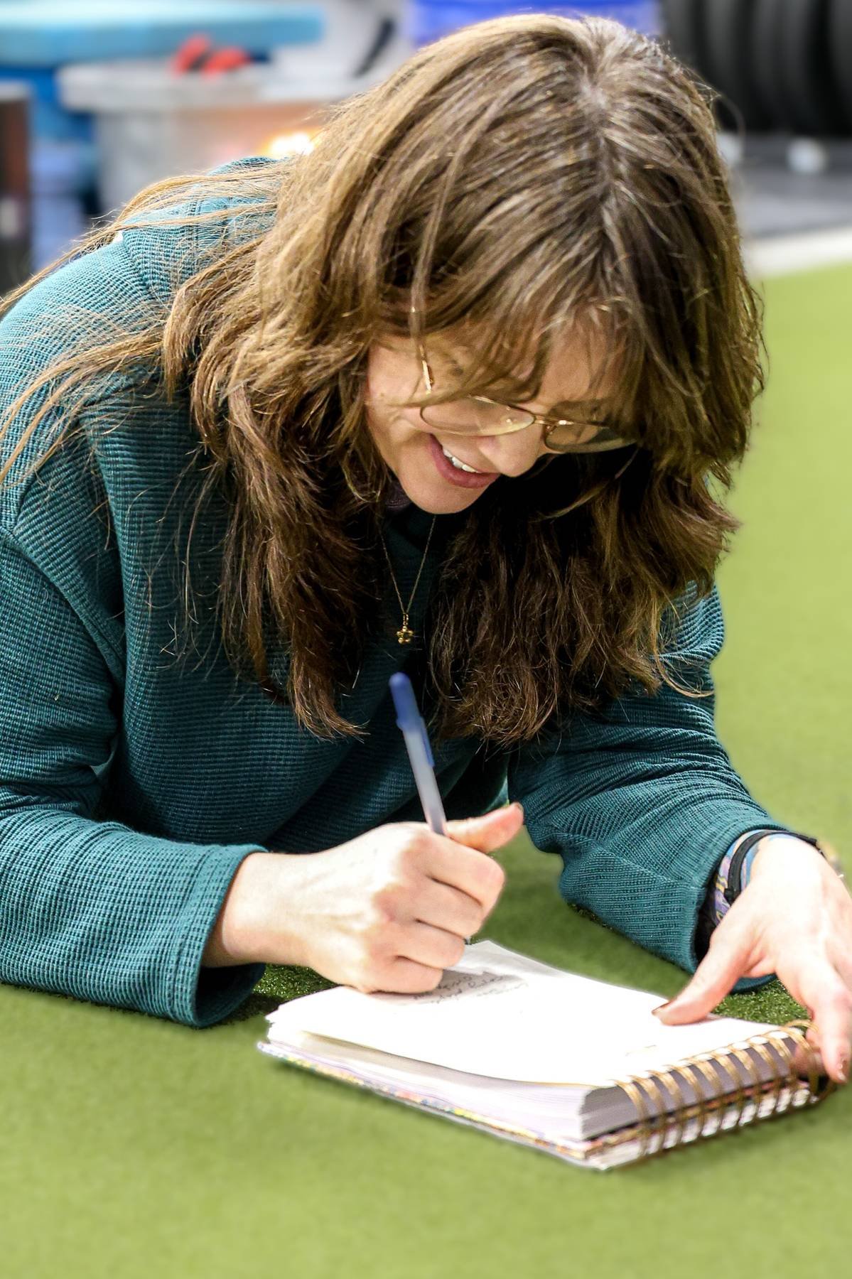 A woman is smiling and writing in a notebook