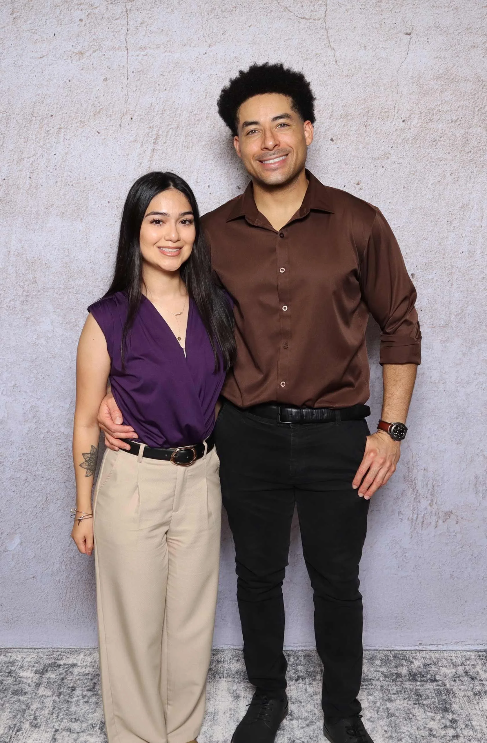 Professional full-length studio portrait of Ryan and Jezebel, co-owners of Perfect Capture Booth, standing together in front of a textured neutral backdrop.