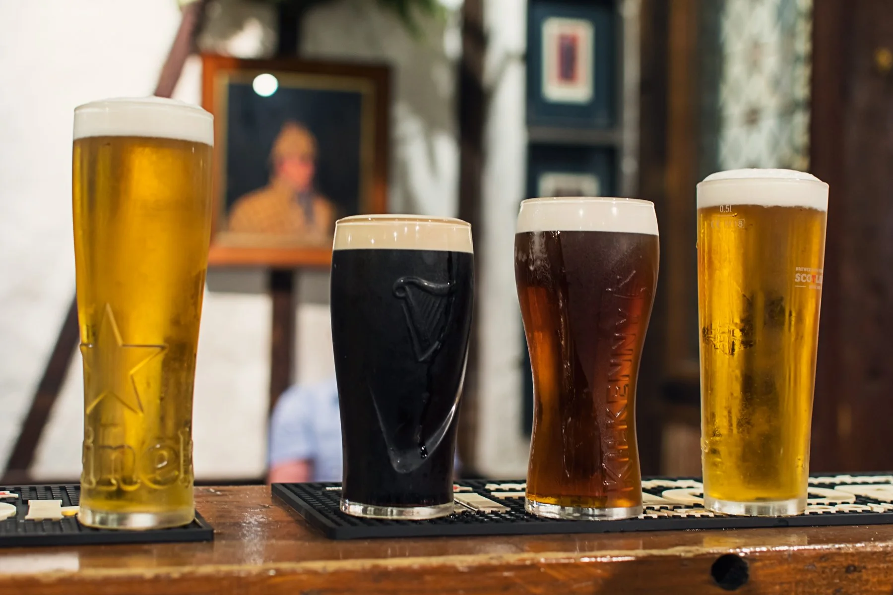 Four pints of beer in various glasses on a bar counter.