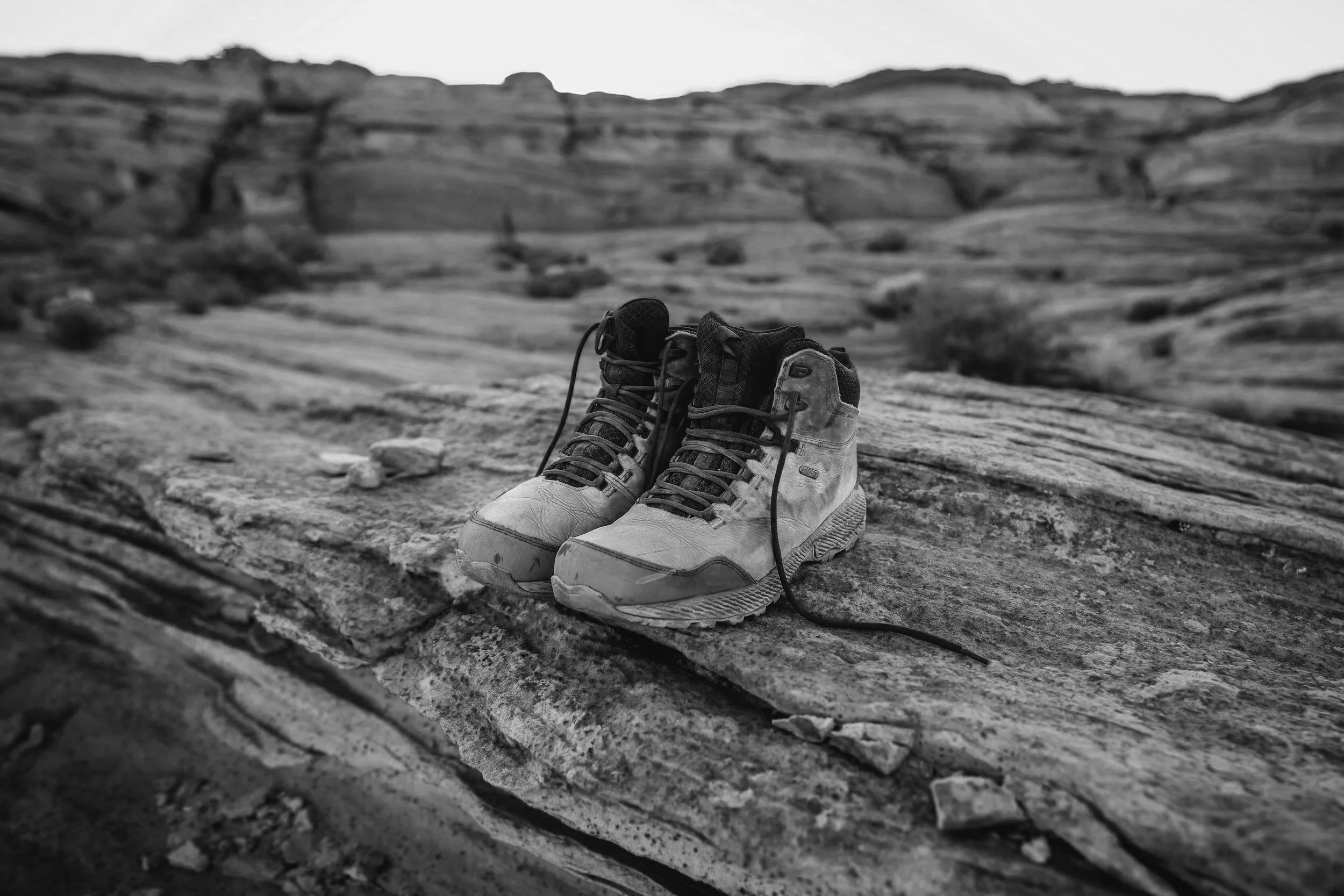 Pair of worn hiking boots placed on a rocky surface in a natural landscape.