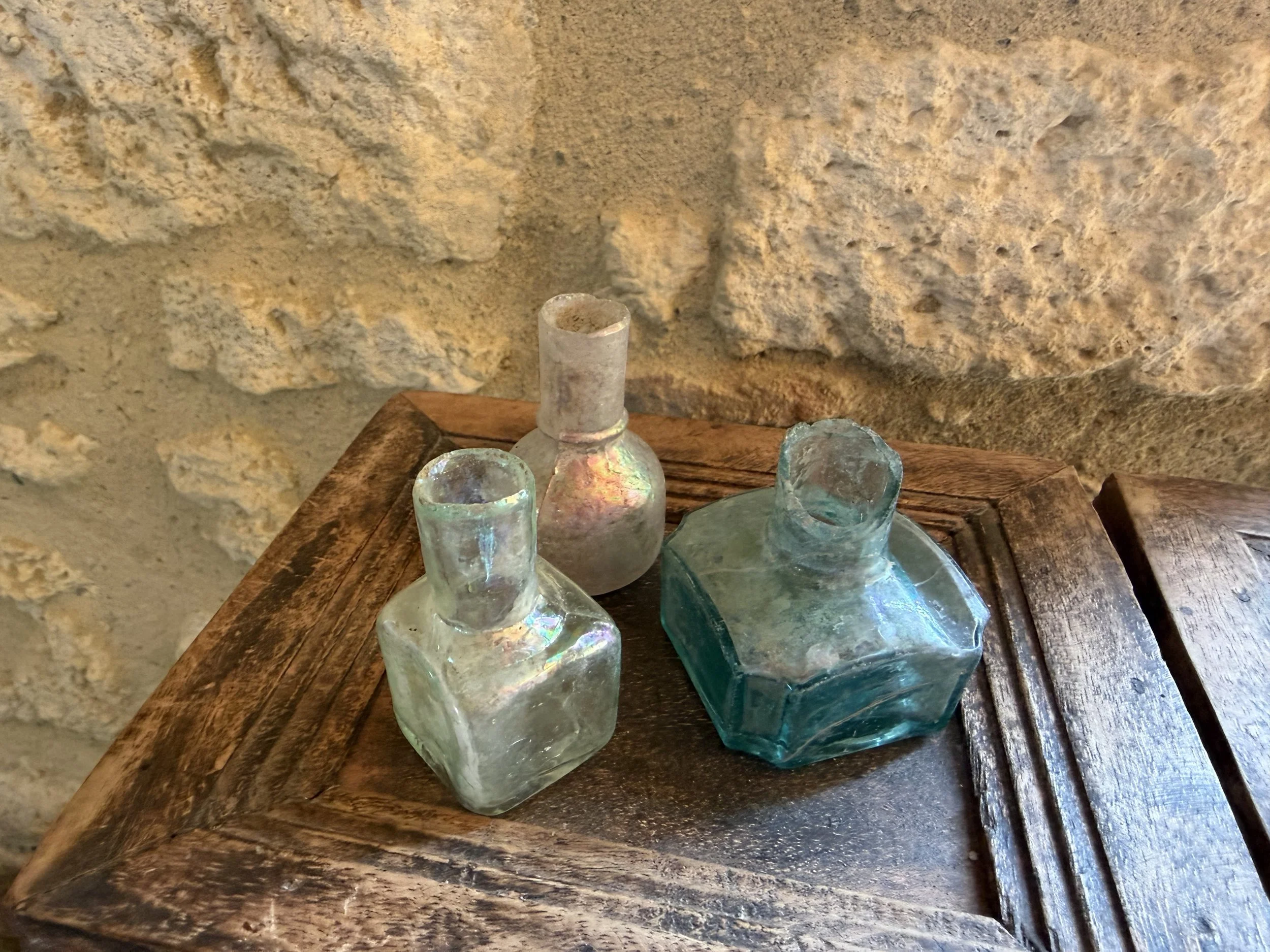 Alte Glasfläschchen auf Holztisch vor Natursteinwand als Symbol für Ruhe, Vertrauen und einen geschützten Gesprächsraum.