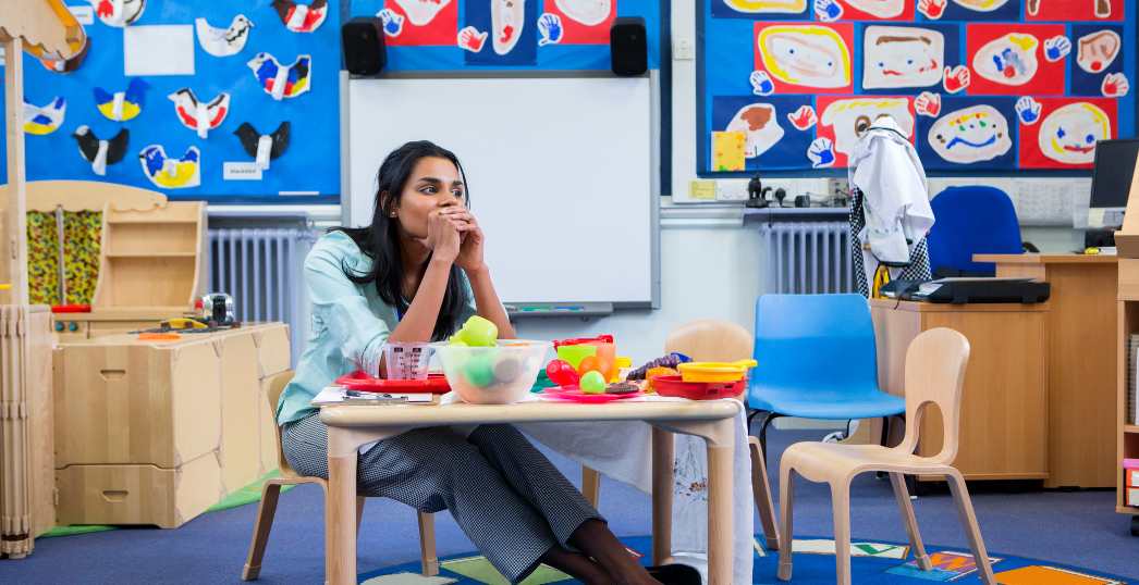 Photo of a stressed Nursery Headteacher sitting in a classroom. She is sitting at the toy table.
