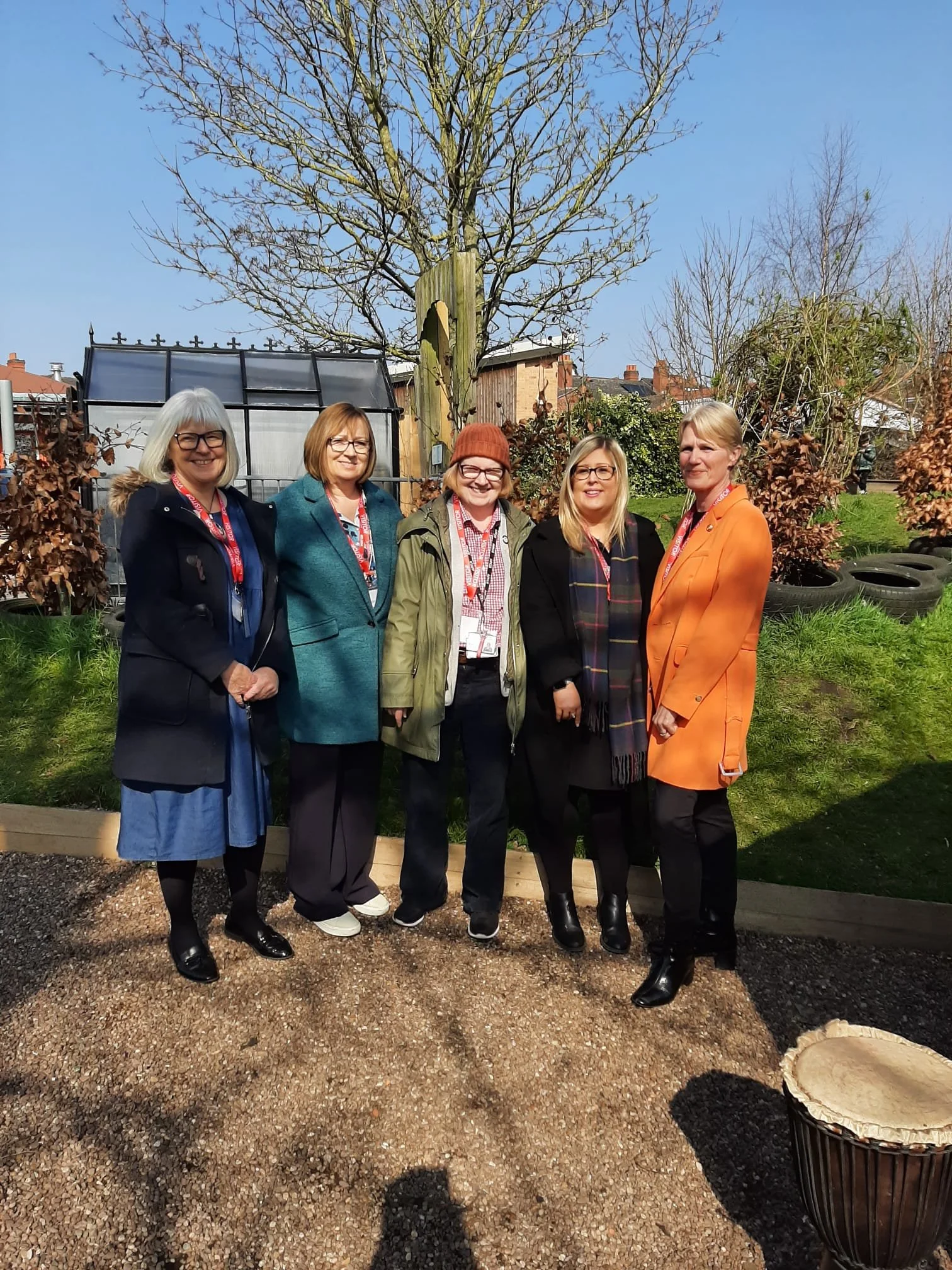 A groupf of 5 white women stand in a garden, looking at the camera and smiling
