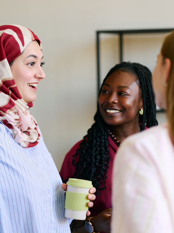 A group of diverse women talking during a workplace leadership meeting, holding coffee.
