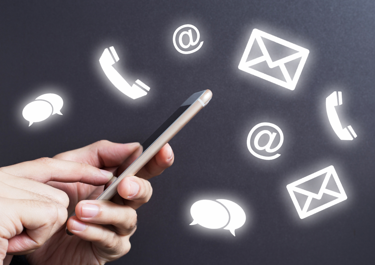 Close up shot of a hand holding a smart phone with communications icons floating around the found - chat, phone, email.