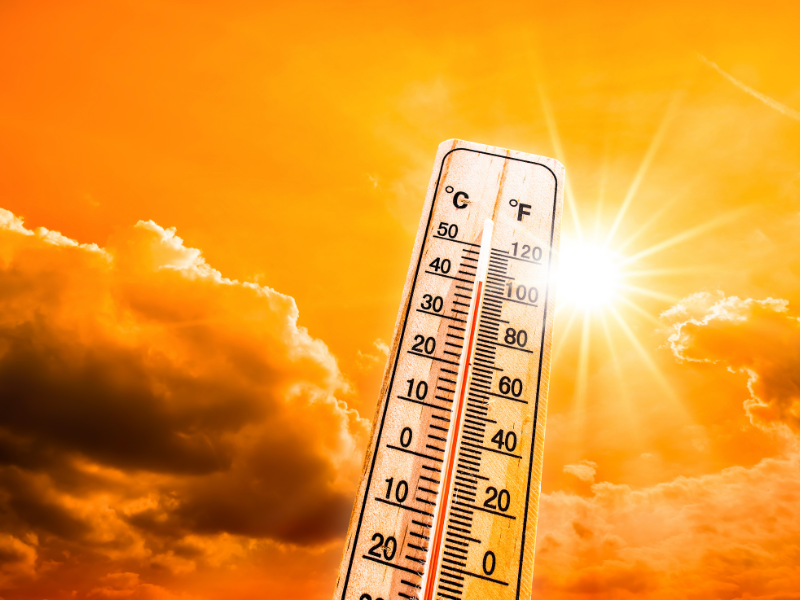 Concept graphic of a heatwave: Close-up of a thermometer on a glowing orange background with bright sun