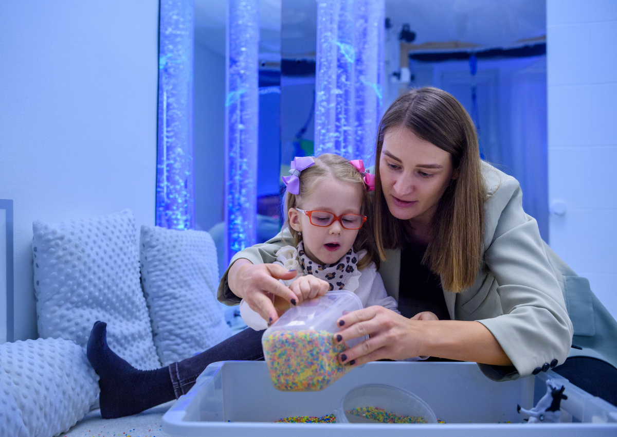 An early years practitioner support a child with additional needs in their play in a sensory room