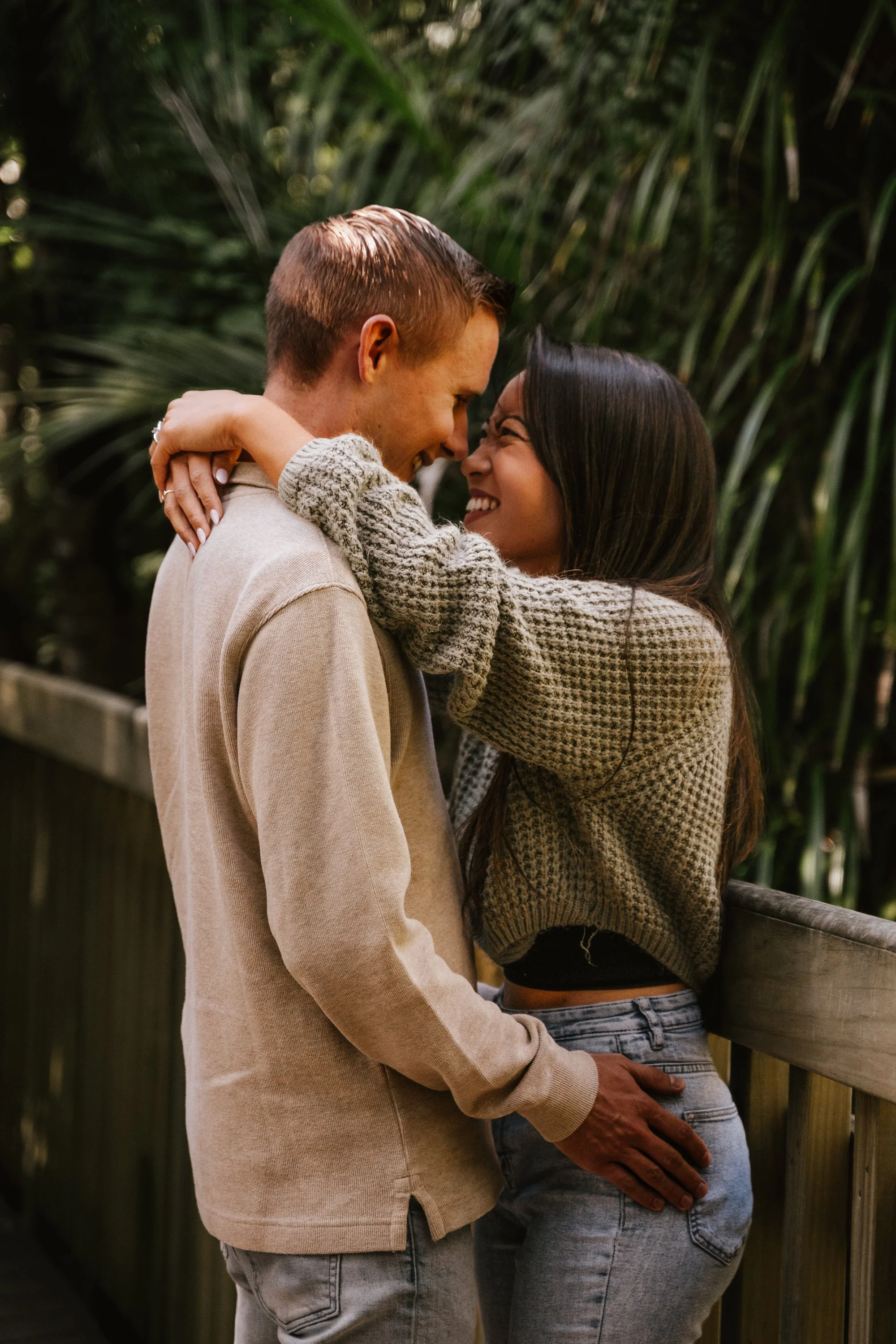 A couple embracing and smiling outdoors, with greenery in the background.
