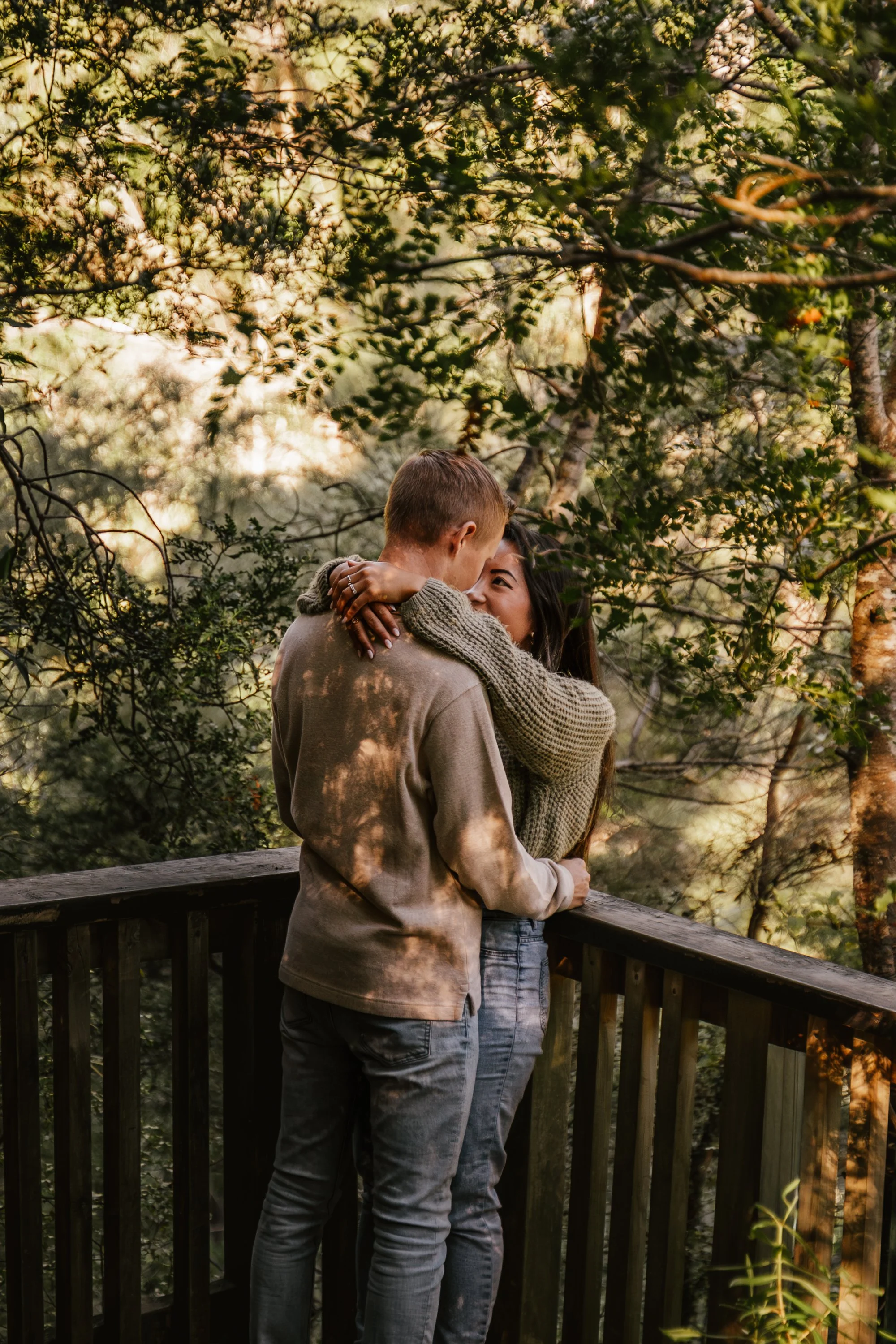 A man and woman embracing each other on a wooden deck surrounded by trees and greenery.