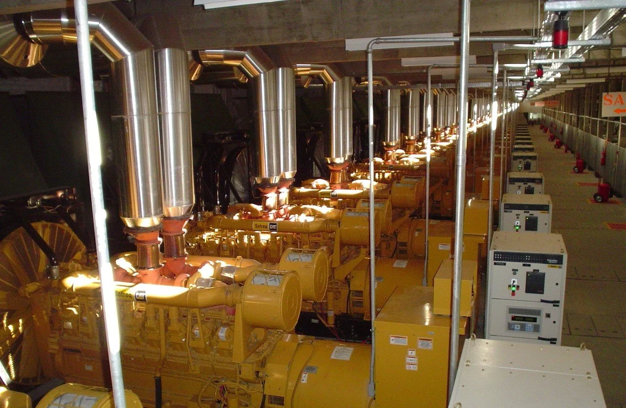 Large industrial generators with yellow and metallic components in a power plant or electrical facility.