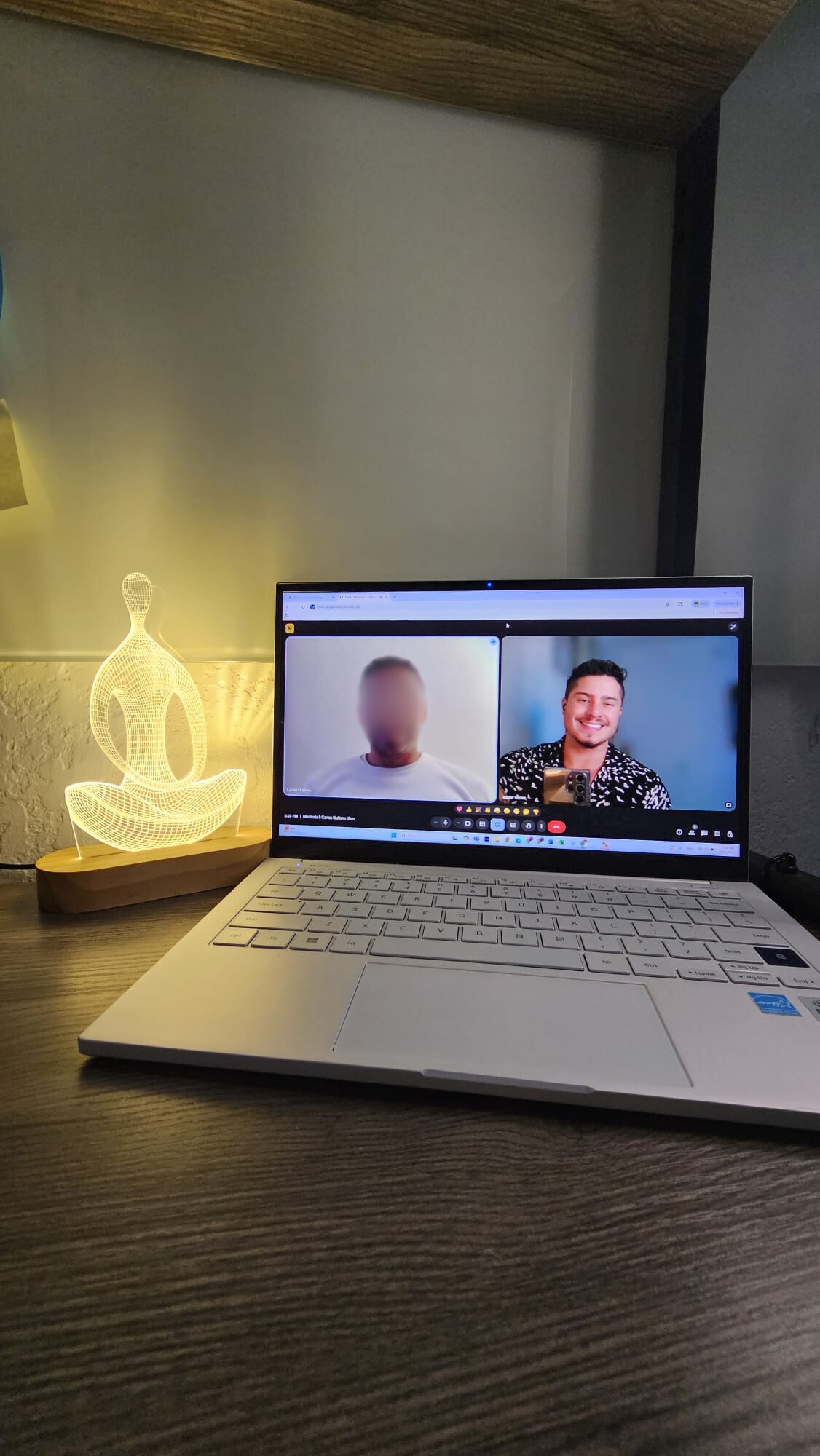 A screenshot of a video call showing a woman and two men, with the woman in the background, at the top, and two men in separate video windows, one on top of the other, with the top man in a gray shirt taking a selfie and the bottom man with a blurred face.