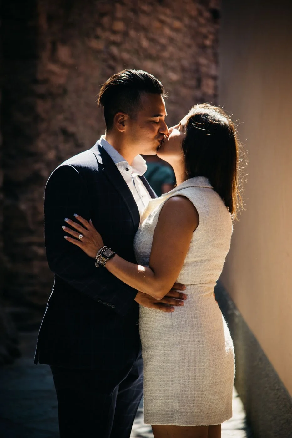 A couple is embracing and sharing a kiss indoors, with warm lighting highlighting their faces.