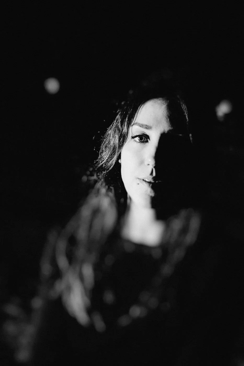 A black and white photo of a woman with half of her face illuminated, with water and bubbles in the foreground.