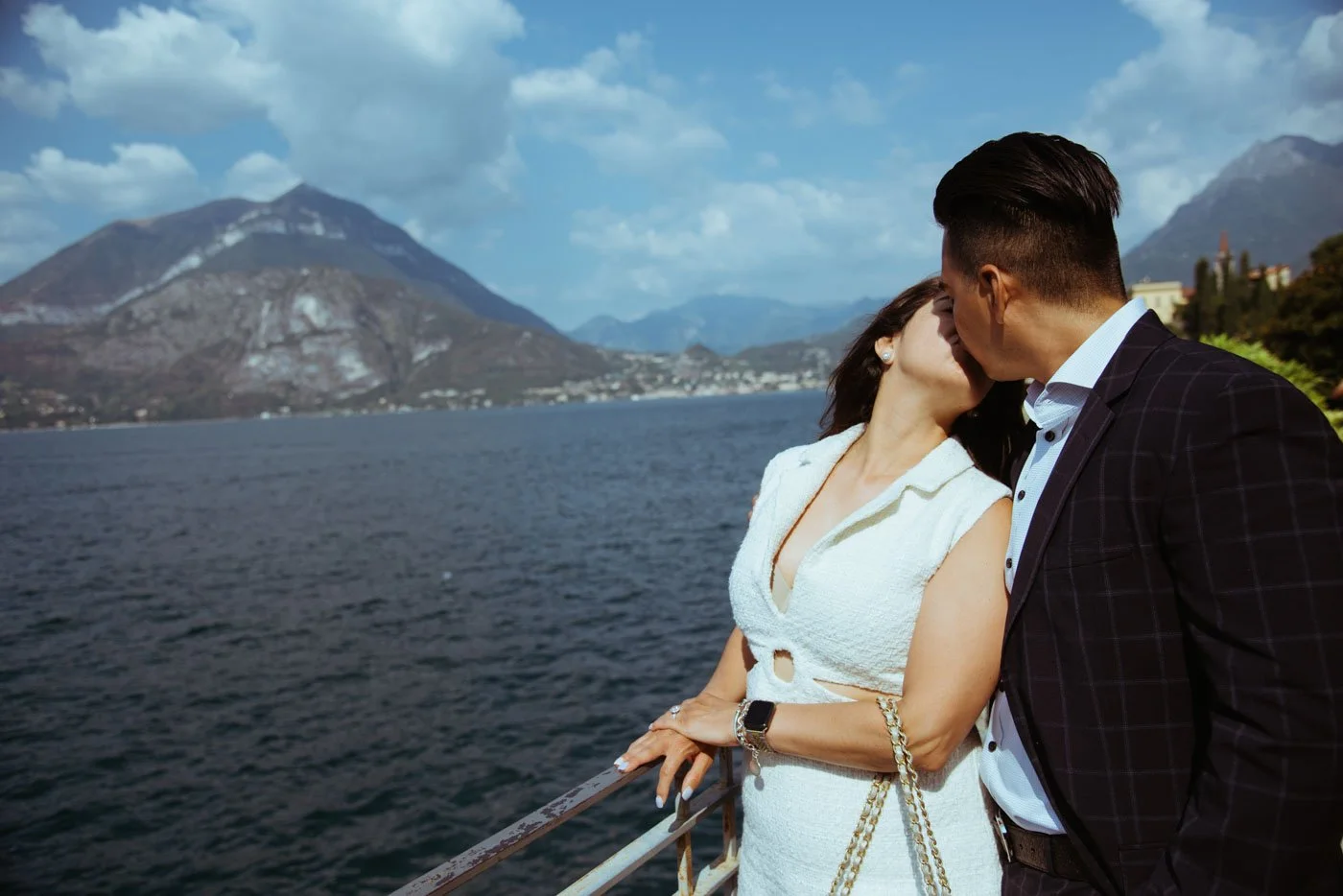 A couple sharing a kiss on a boat with a lake and mountains in the background.