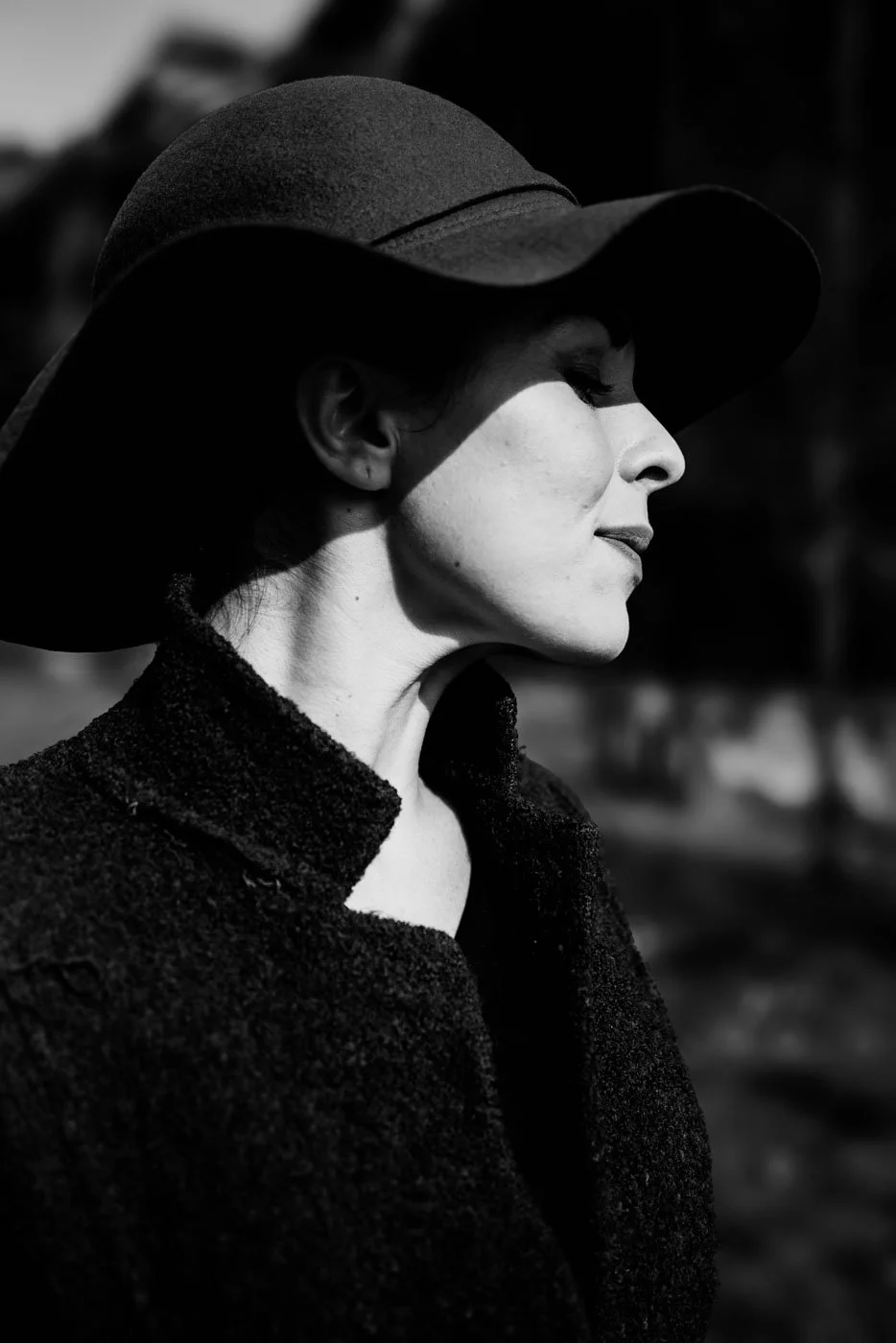 Profile of a woman wearing a wide-brimmed hat and textured coat, looking to the side in black and white.