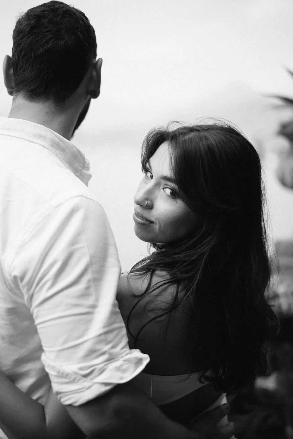 A black and white photo of a man and woman facing each other, the woman looking at the camera with a slight smile.