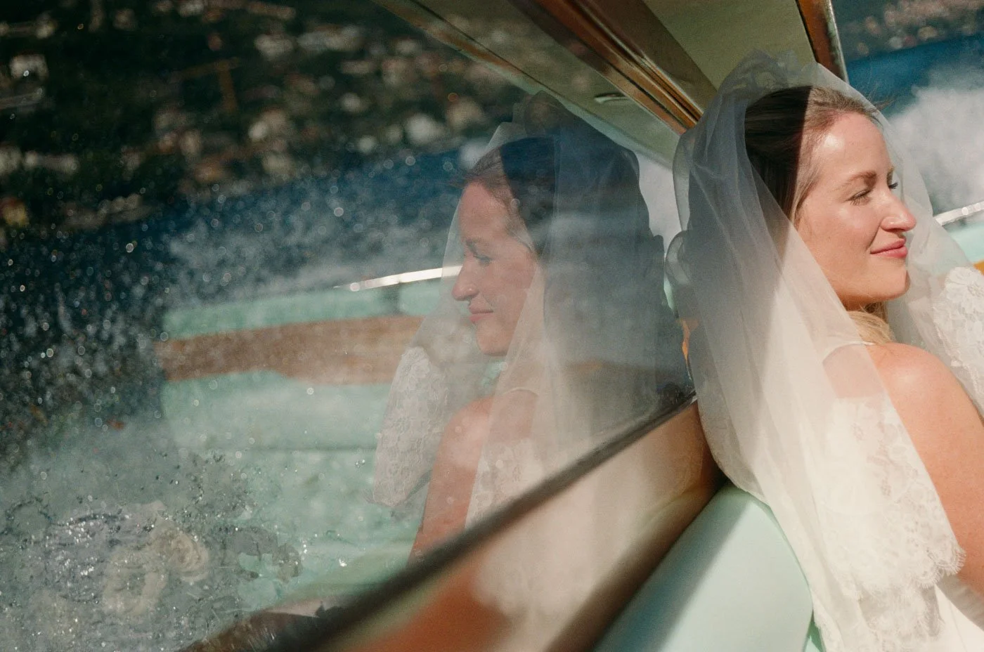 A bride sitting in a car with her eyes closed and a peaceful smile, reflected in the window.