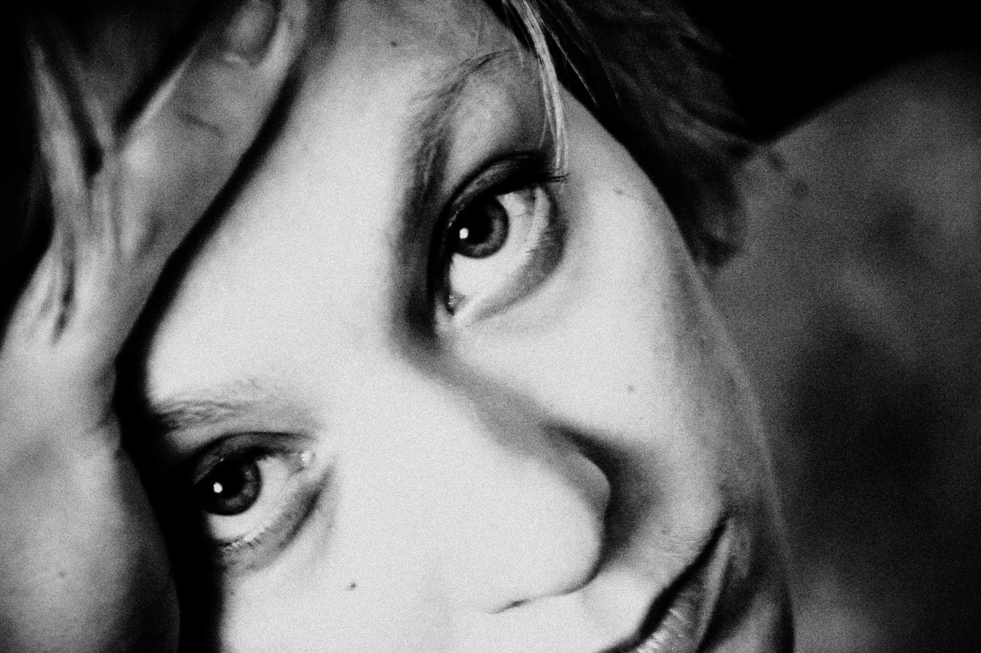 Close-up black and white photo of a woman's face, focusing on her eyes and lips, with her hand gently touching her forehead.