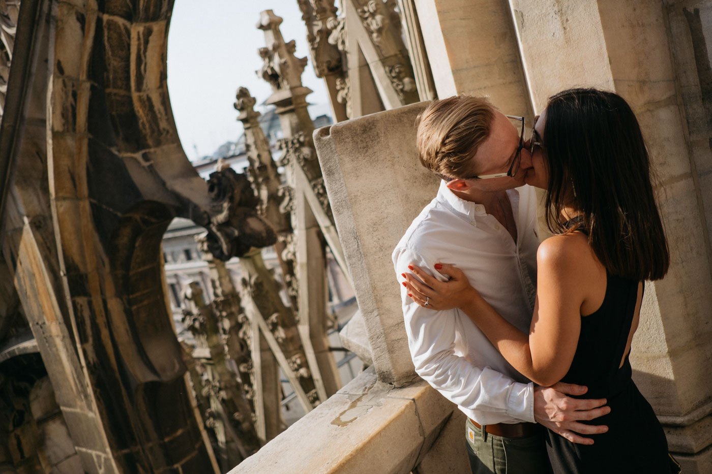 A couple kissing on a rooftop terrace in front of ornate architectural details of a historic building.