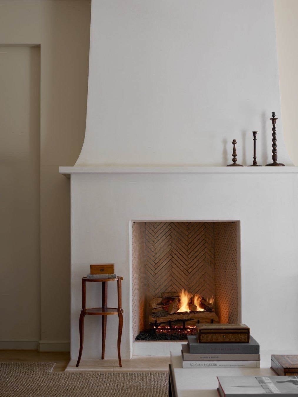 Living room with a white fireplace, lit with a fire, decorated with books and candlesticks.