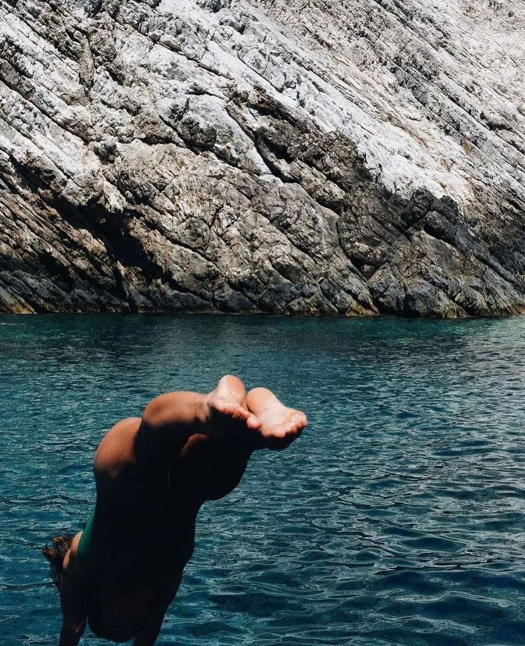 Person diving into the water near a rocky cliff