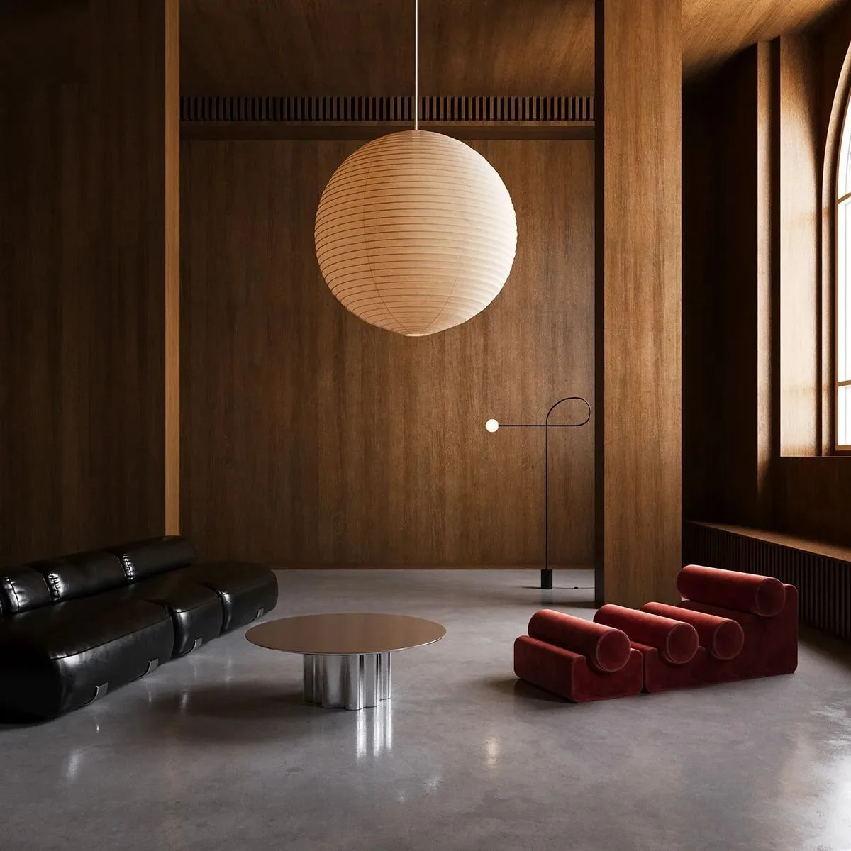 Minimalist living room with black leather sofa, round coffee table, red velvet lounge chair, wood-paneled walls, large window, and hanging paper lantern light.