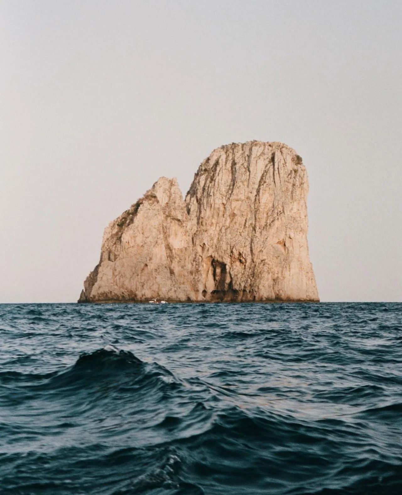 Large rocky island protruding from the ocean with deep blue water and a clear sky.