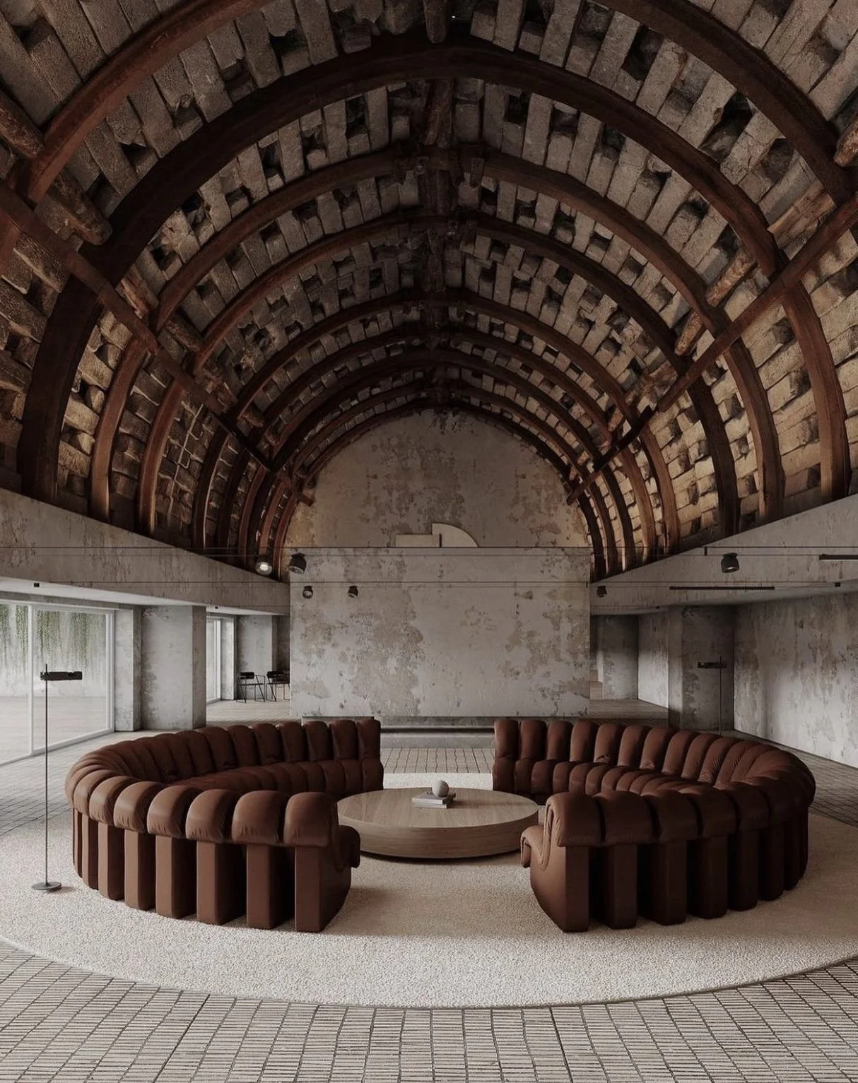 Interior of a modern space with a curved brown sofa arranged in a circle around a round wooden coffee table, with large windows and a vaulted brick ceiling.