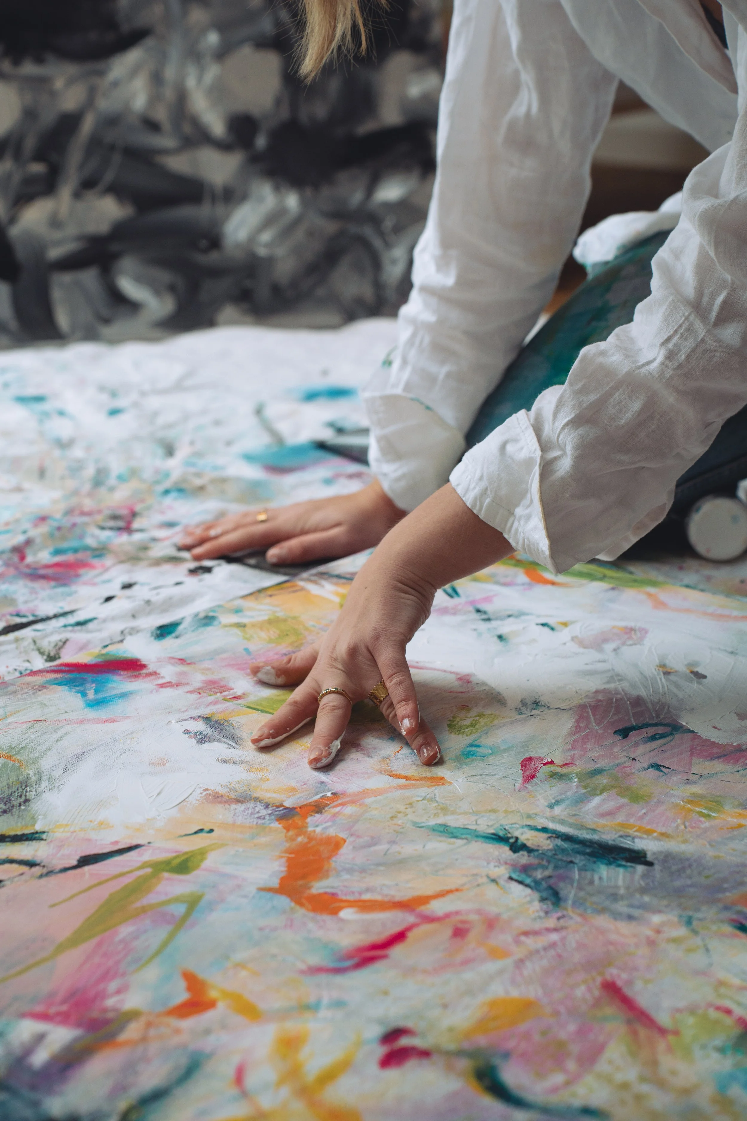 Person with painted hands creating abstract art on a large canvas on the floor.