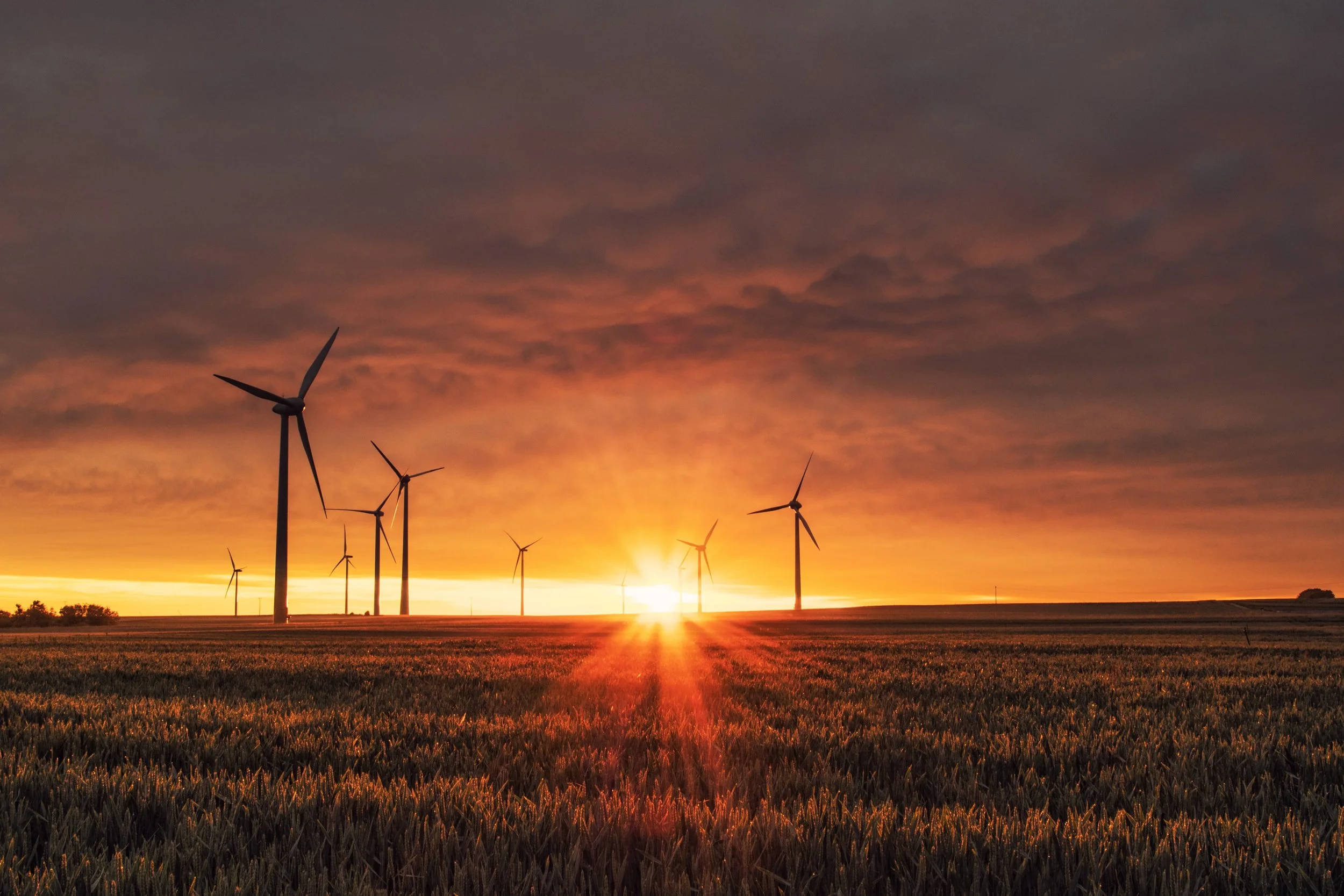 Wind turbines at sunset over a field with orange sky.