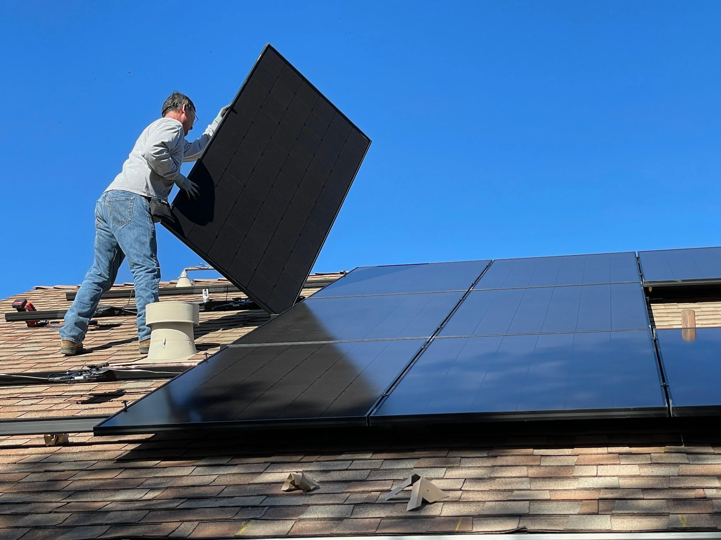 Person installing solar panels on a rooftop under clear blue sky.