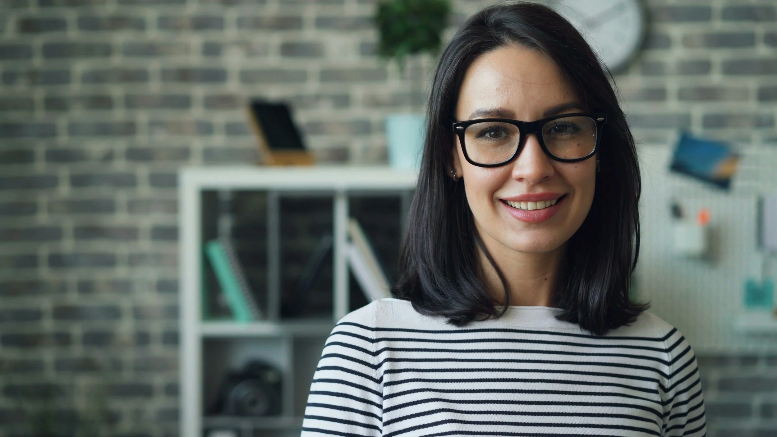 Woman with glasses smiling in a modern office.