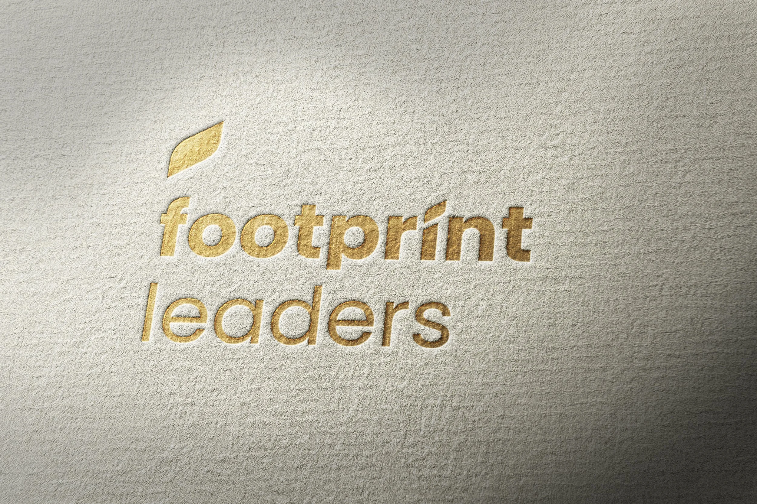 Embossed logo with the words "footprint leaders" and a leaf icon on textured paper surface.