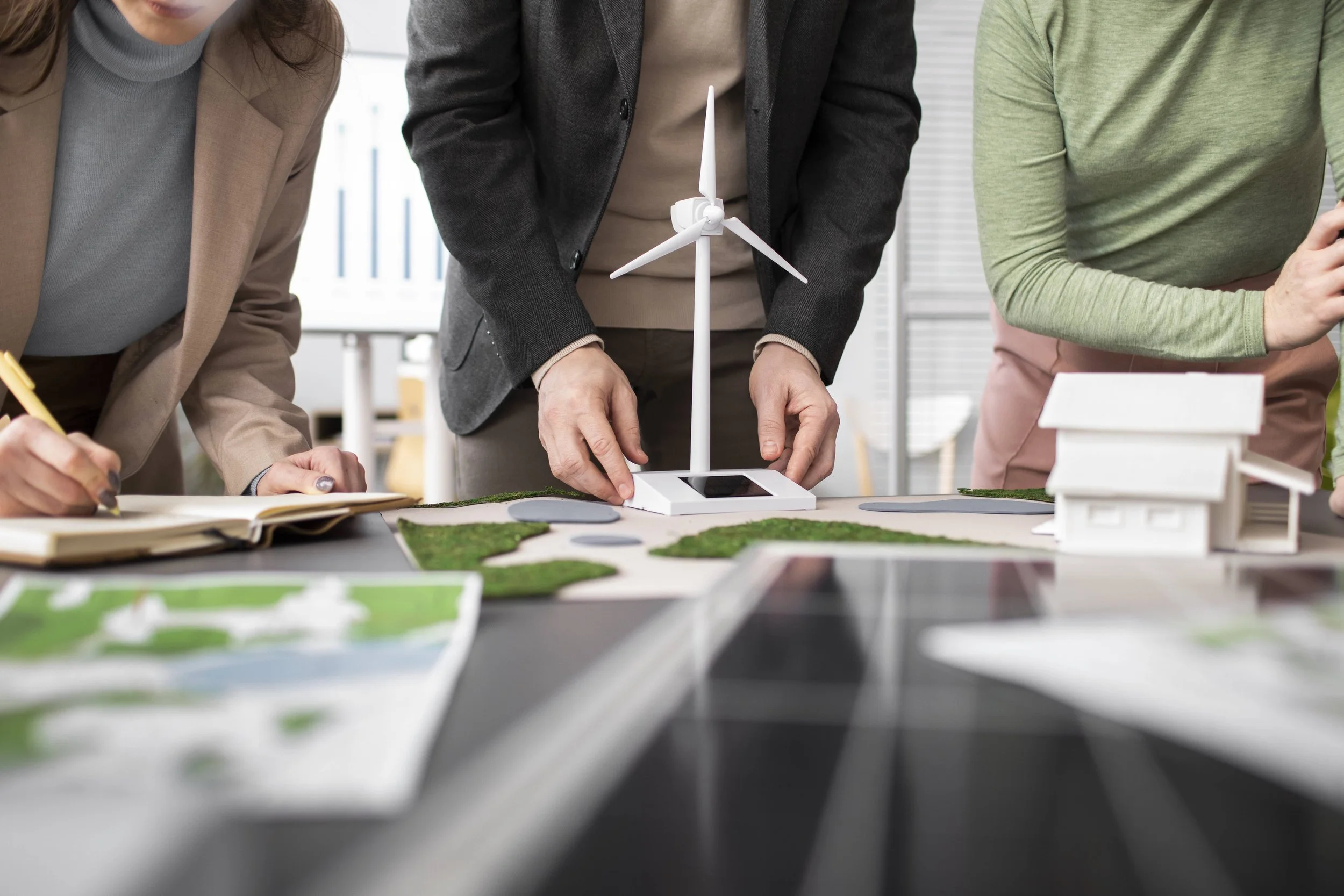People working on a renewable energy project with wind turbine model and architectural models on a table.