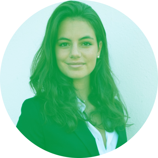 Smiling person with long hair wearing a suit, standing against a plain background.