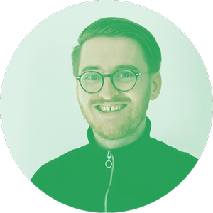 Porträt einer lächelnden Person mit Brille und kurzen Haaren, die eine grün gefärbte Jacke mit Reißverschluss trägt.