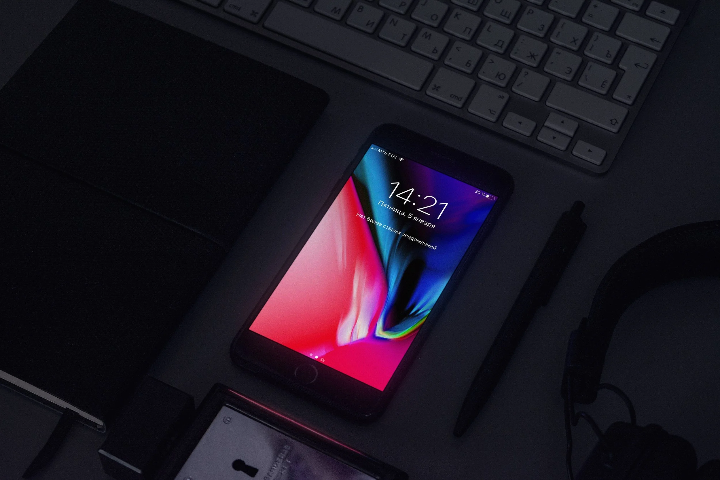 Smartphone on desk with keyboard, notebook, pen, and headphones.