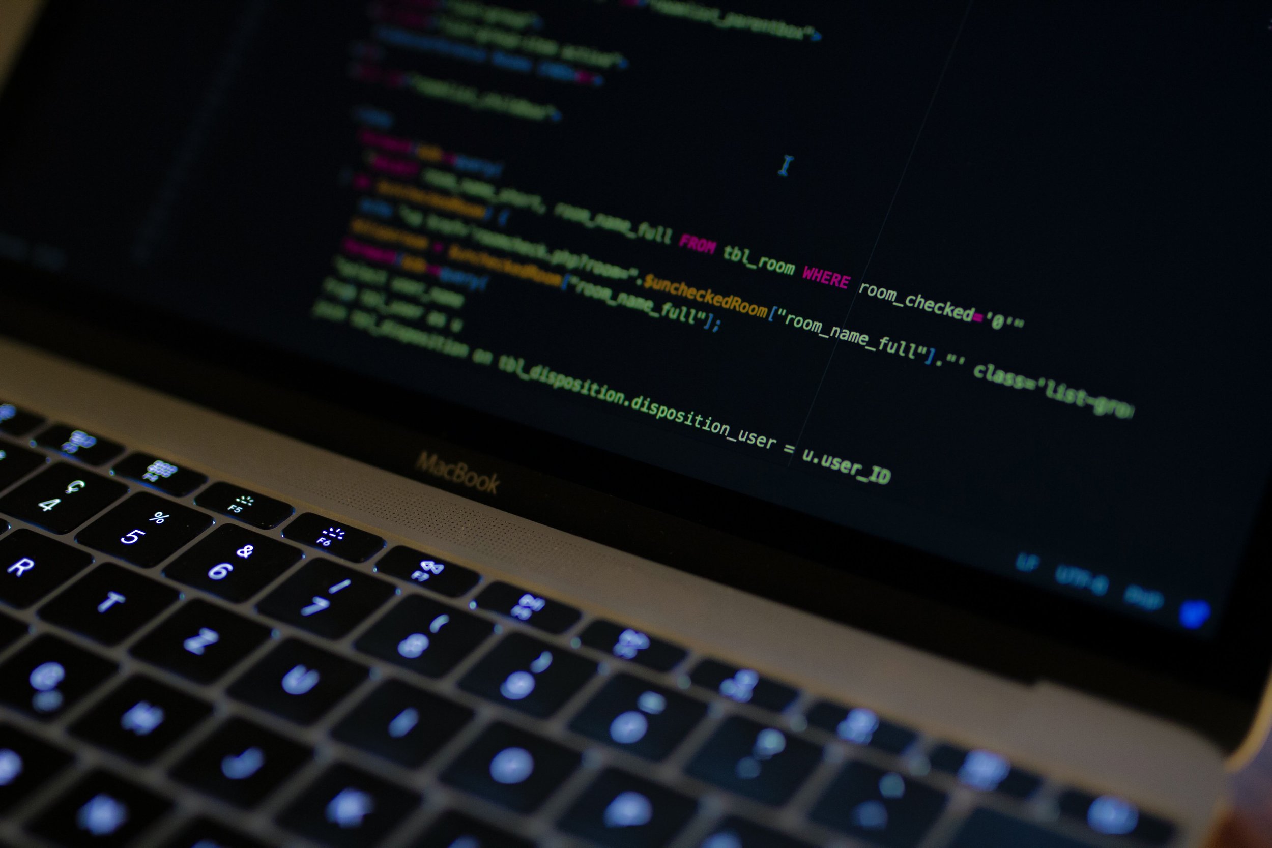 Close-up of MacBook screen displaying computer code with a backlit keyboard.