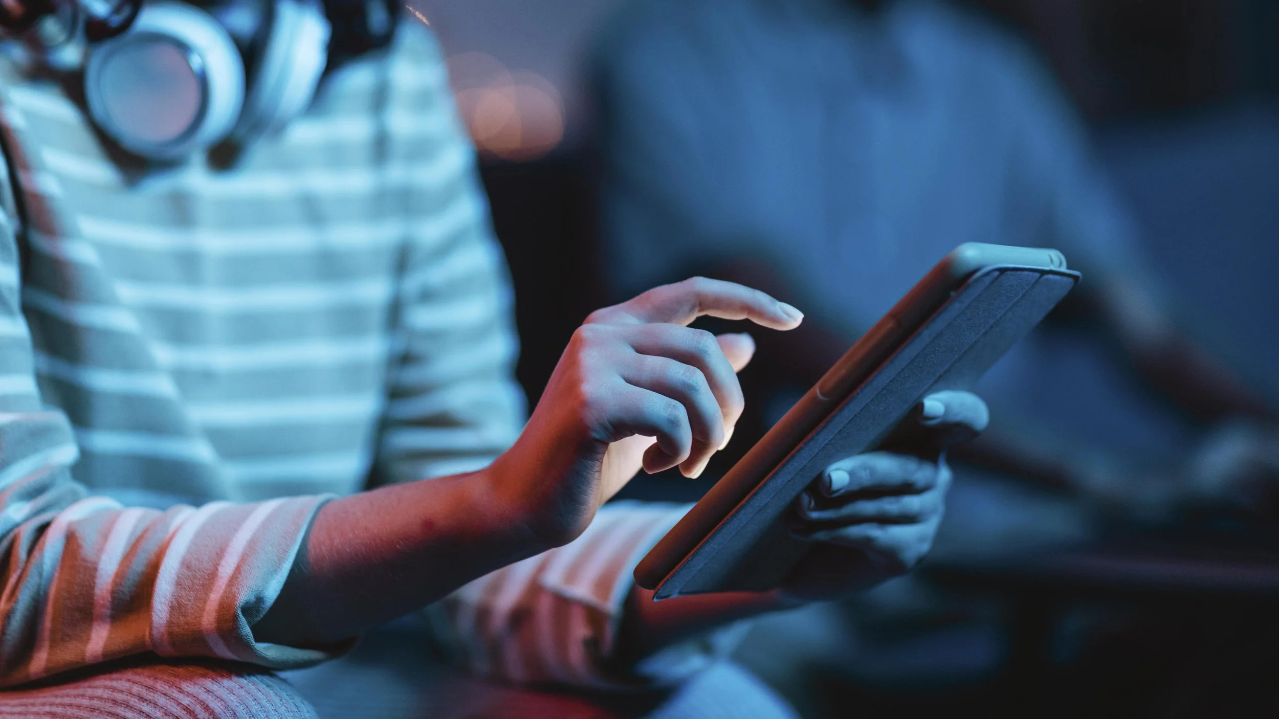 Person using a tablet with headphones around neck, wearing a striped sweater.