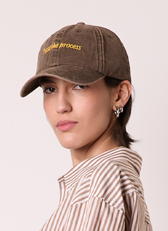 Person wearing a brown baseball cap with "subtle process" written on it in yellow text, and a striped shirt.