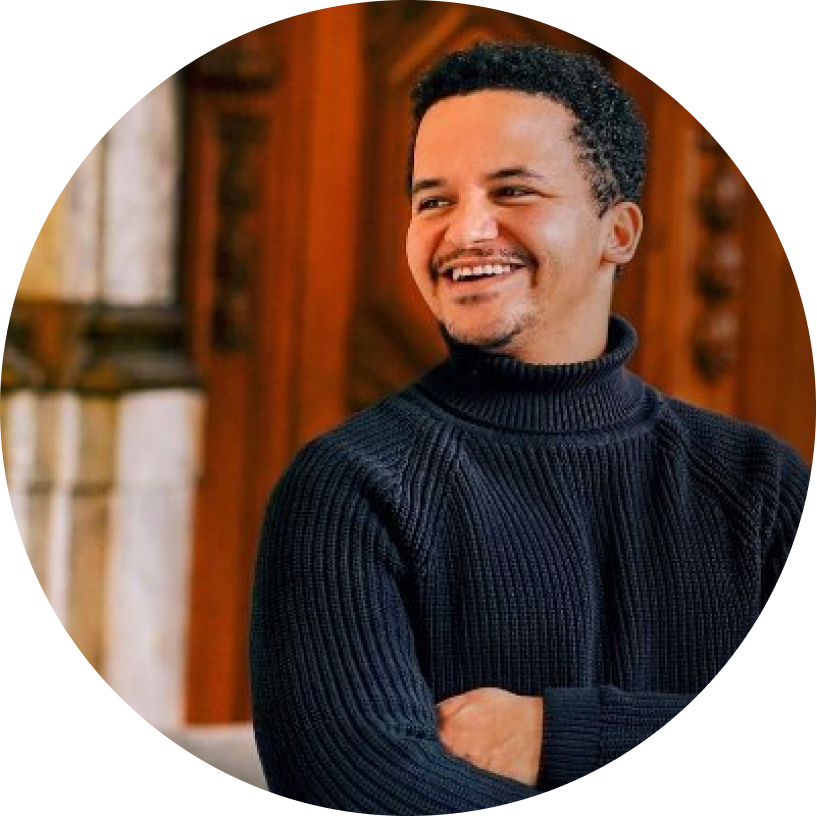 Smiling person wearing a black turtleneck in front of a wooden background.