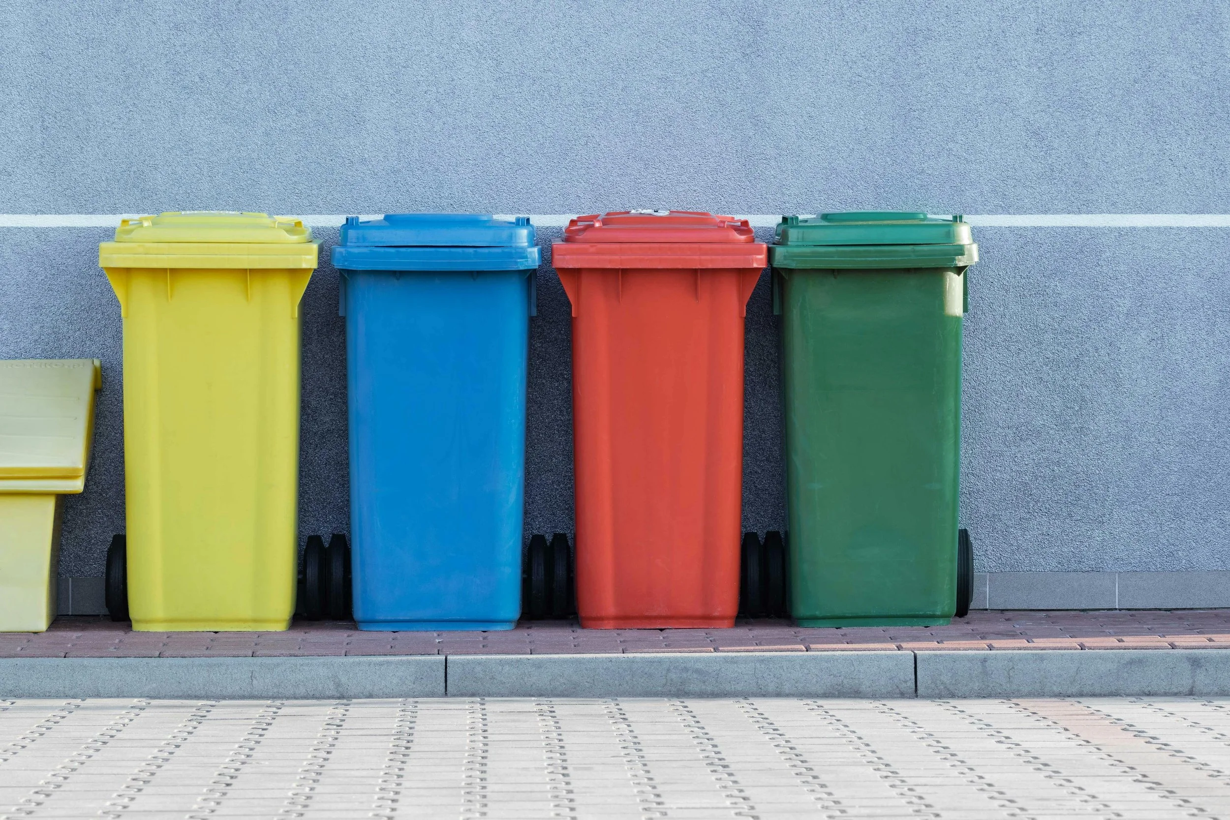 Four colorful trash bins lined up against a gray wall