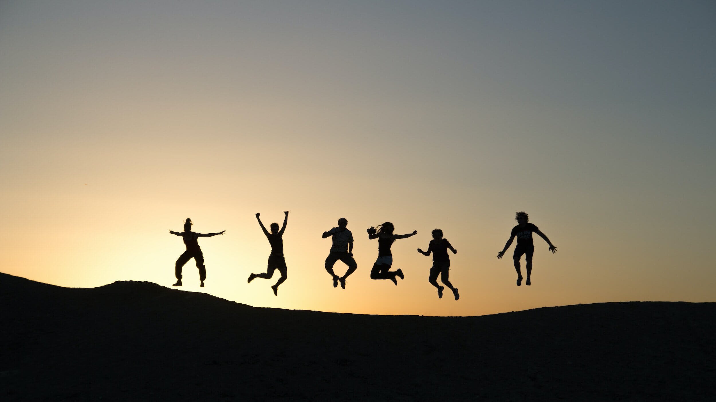 Silhouetted group of people jumping at sunset