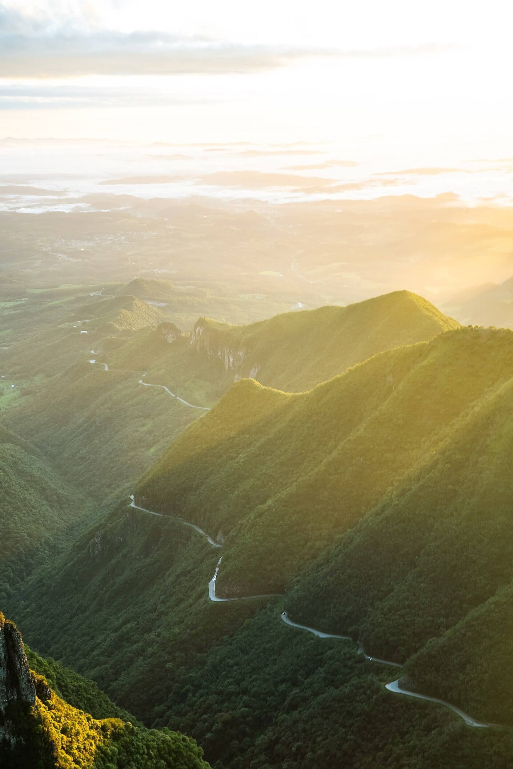 Aerial view of lush green mountains with a winding road during sunrise.