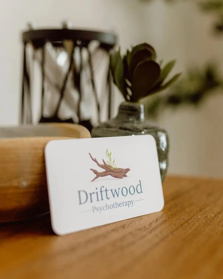Driftwood Psychotherapy business card on a wooden table beside a glass vase with greenery