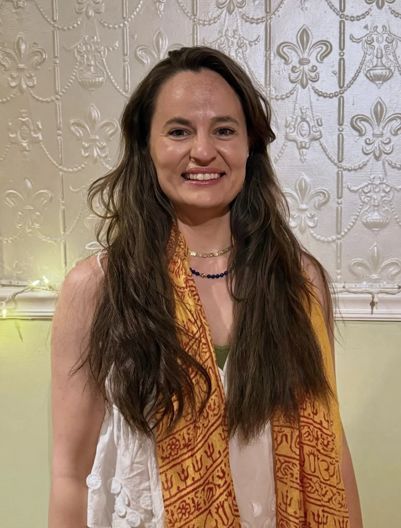 yoga teacher with long brown hair smiling against a white wall.