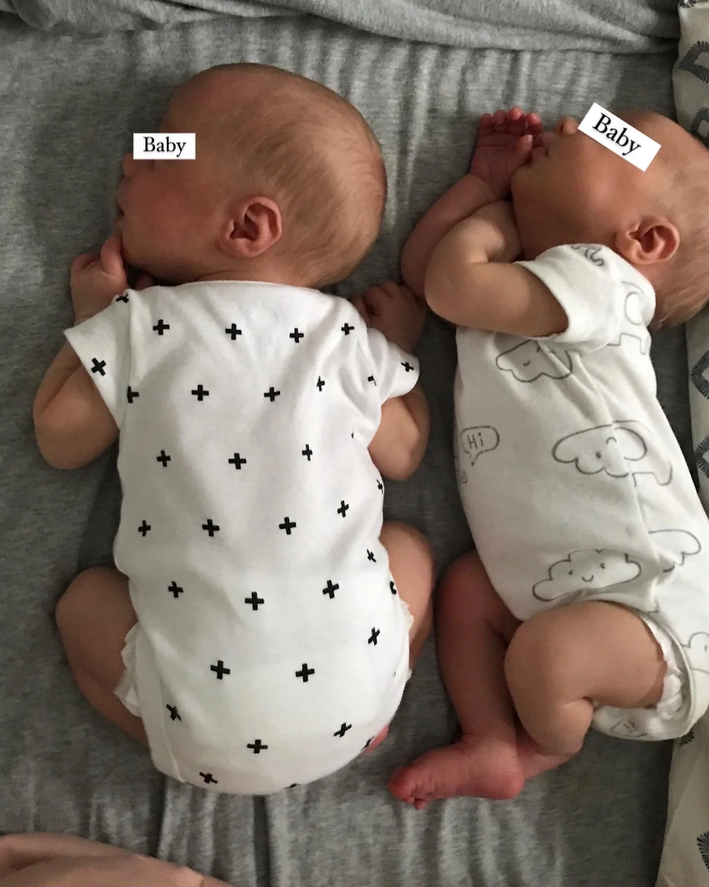 Two babies lying on their sides wearing onesies; one with a black cross pattern and the other with cloud designs.