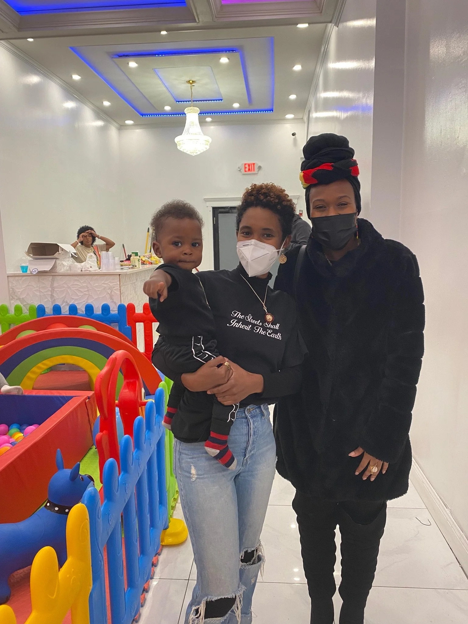 Two adults and a child indoors near colorful play equipment, with a bright ceiling light above.