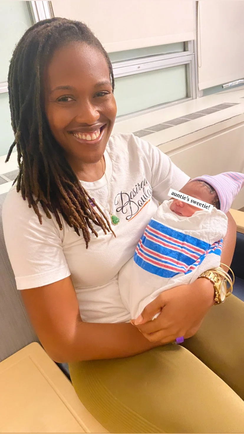 Smiling woman holding a newborn wrapped in a hospital blanket.