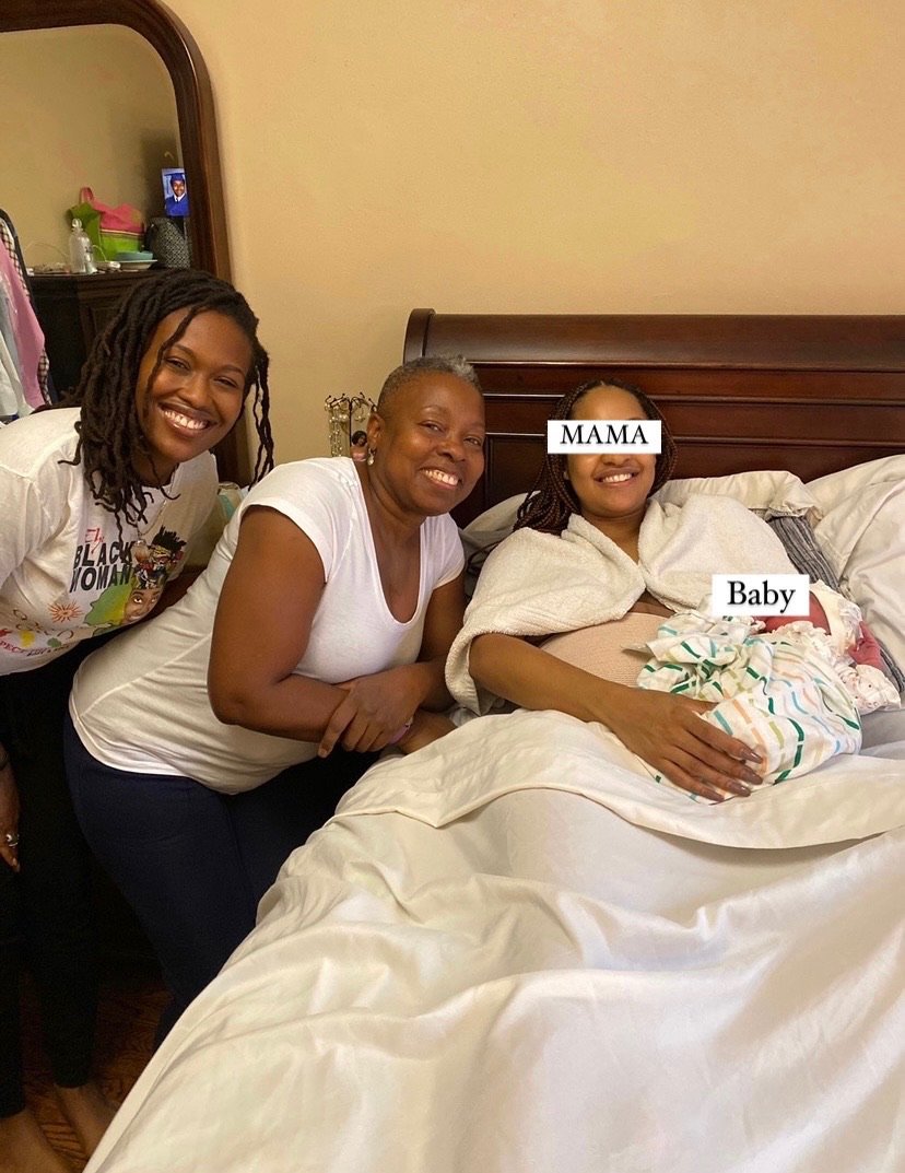 A family scene with three women and a newborn baby. Two women are smiling at the camera, while one woman is lying in bed holding the baby wrapped in a blanket. Labels "Mama" and "Baby" are edited onto the image.